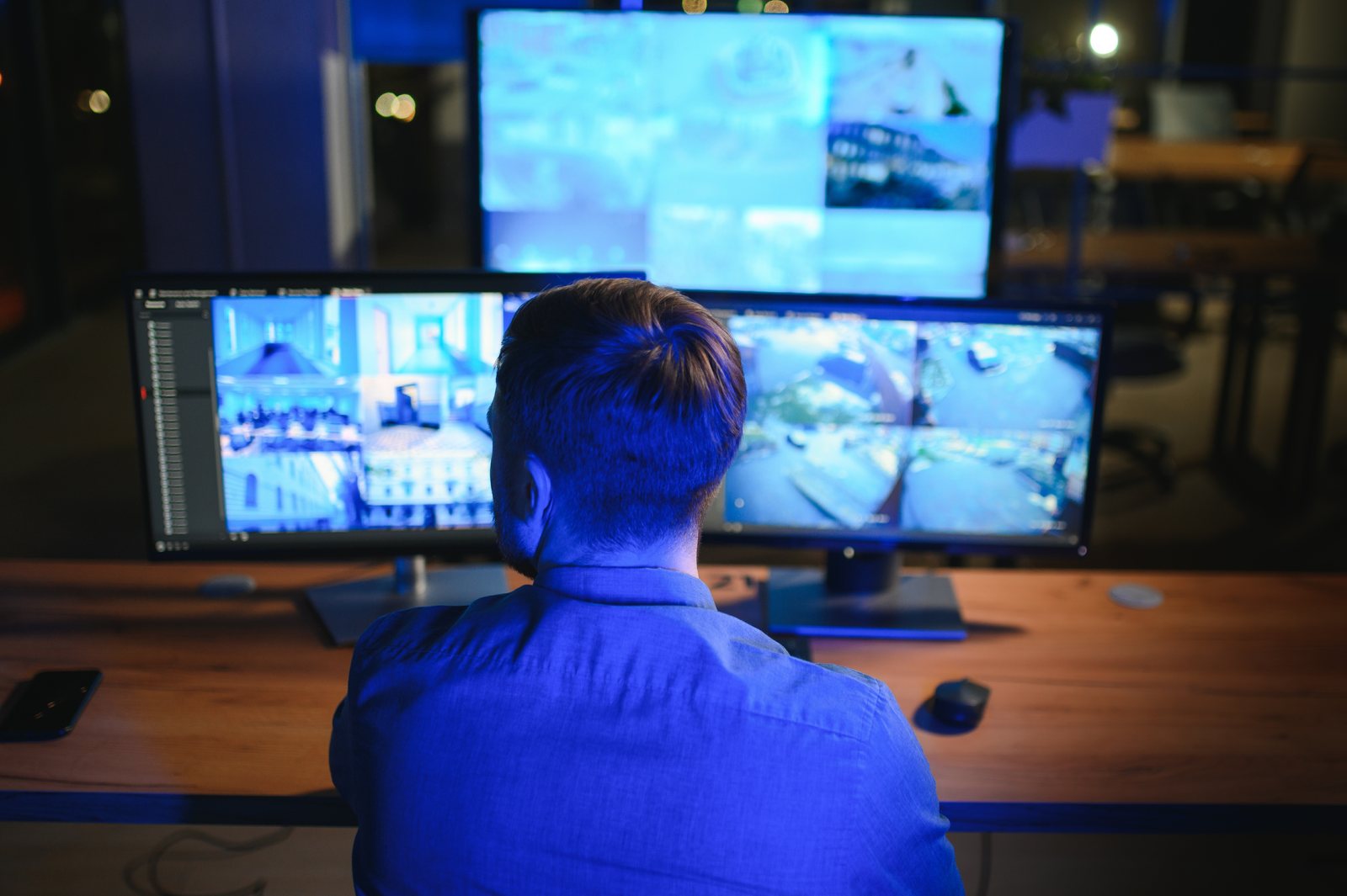 Opérateur de dos devant trois écrans de vidéosurveillance